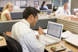 2161075-businessman-in-cubicle-at-laptop-eating-sushi