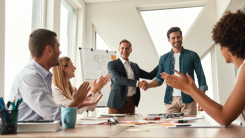 Good job! Two cheerful colleagues shaking hands and smiling while having a meeting in the modern office